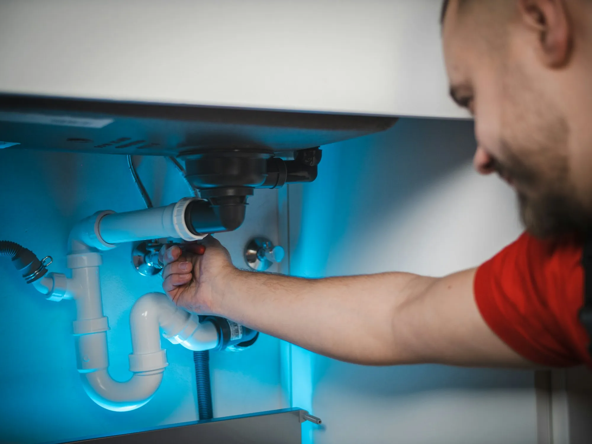 Technician working on water pipes beneath a sink