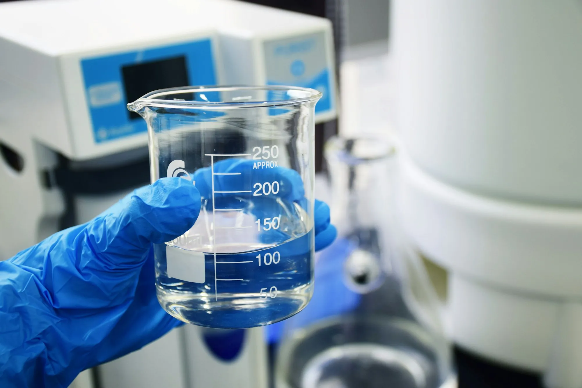 Gloved hand holding a laboratory beaker of water for testing